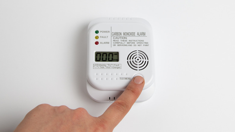 close up of a person's finger testing carbon monoxide alarm