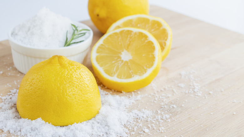 Lemon halves on a wooden board alongside dish and pile of coarse sea salt