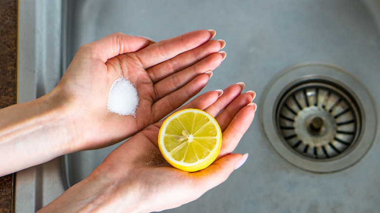 Woman's hands holding lemon half and small pile of salt over stained metal sink