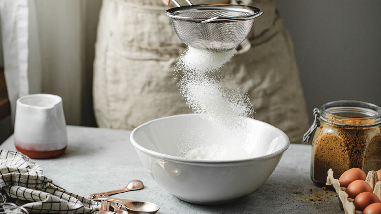 Flour being sifted into bowl next to baking ingredients