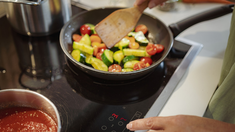 A person cooking a vegetable dish while adjusting settings on an induction stovetop