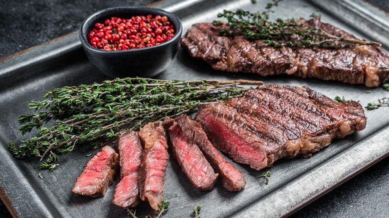 Medium rare charcoal steak with rosemary and pink peppercorns on a black plate.