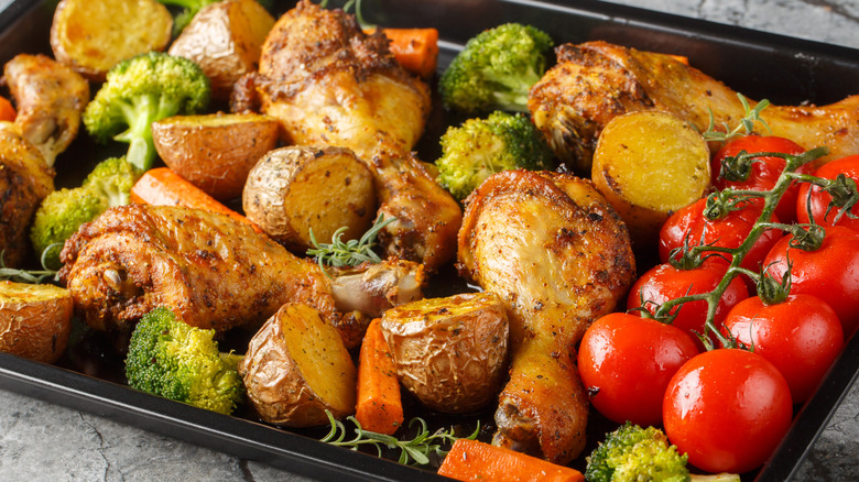 Baking sheet with drumsticks, broccoli, carrots, potatoes, and tomatoes
