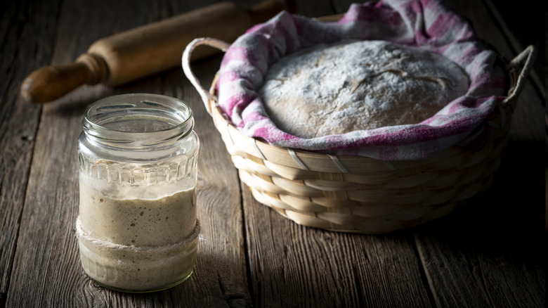 sourdough starter in jar with bread rising in basket