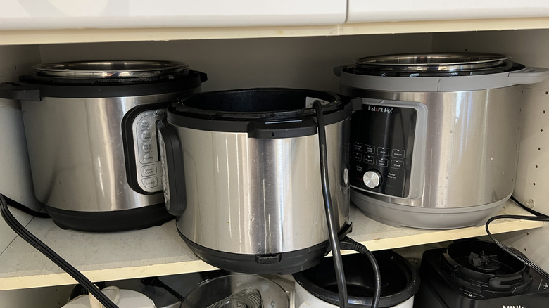 A shelf full of kitchen appliances including several electric pressure cookers