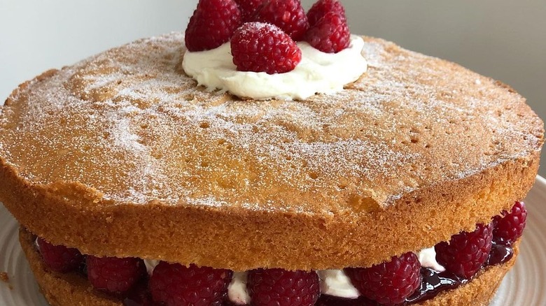 close up of layered sponge cake filled with cream, jam, and fresh raspberries and sprinkled with caster sugar