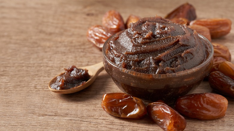 Date paste in bowl next to spoon and whole dates