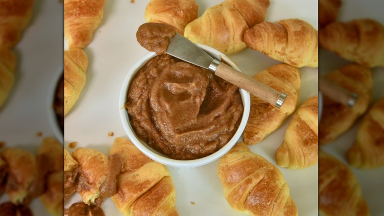 Bowl of date paste with small spatula resting on top, surrounded by croissants