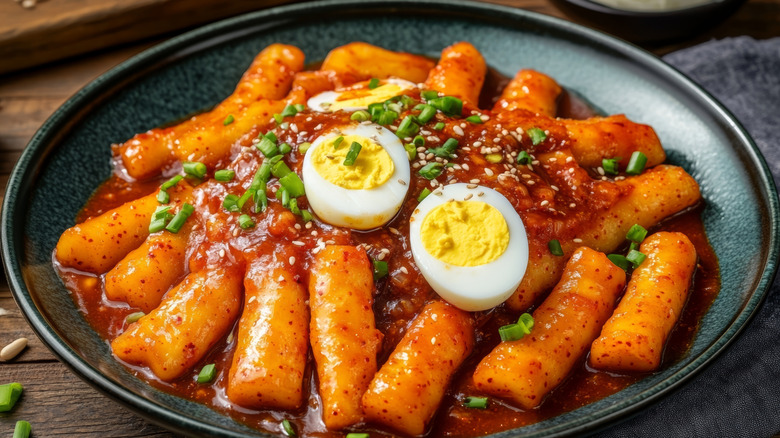 Teokbokki in a plate with plenty of sauce, green onions, sesame seeds, and boiled eggs