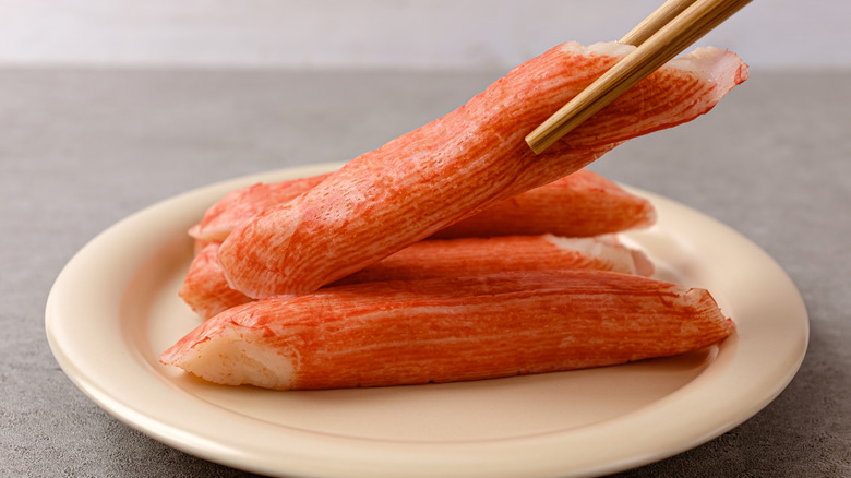 Chopsticks holding up piece of imitation crab over white plate
