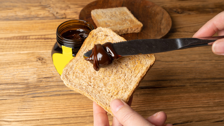 A person spreading Marmite onto slice of bread with a knife