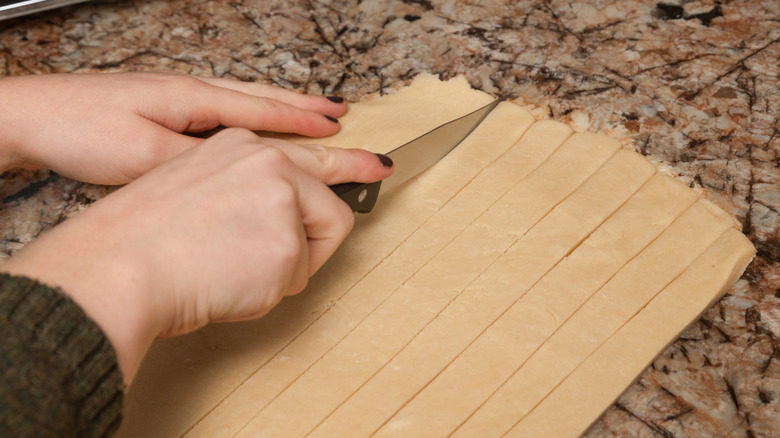 Hands cutting egg noodles on marble counter