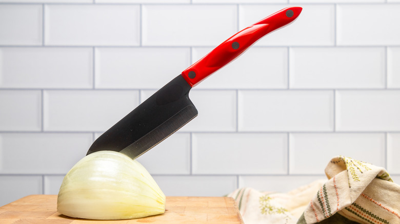 Santoku knife stuck in peeled onion on cutting board
