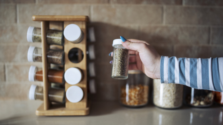 Hand pulling jar out of spice rack on counter