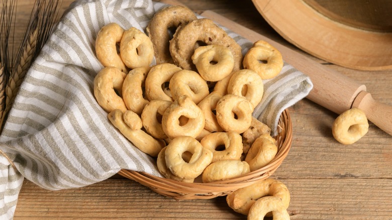 A basket of taralli beside a rolling pin