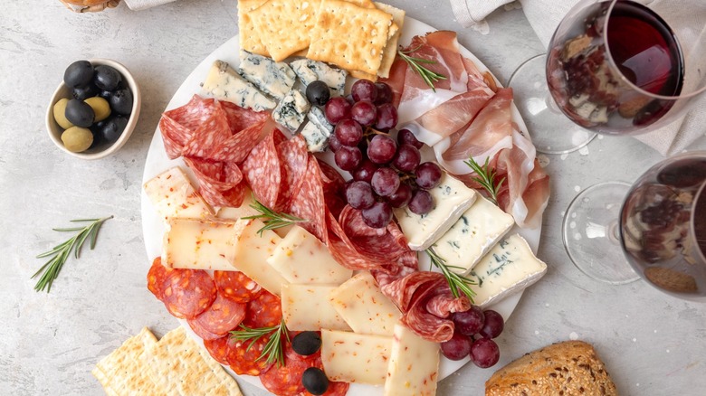 Overview of a charcuterie board beside two glasses of red wine