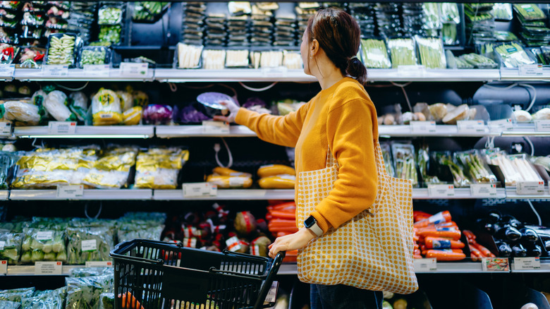 A shopper in a yellow sweater pushing a grocery cart