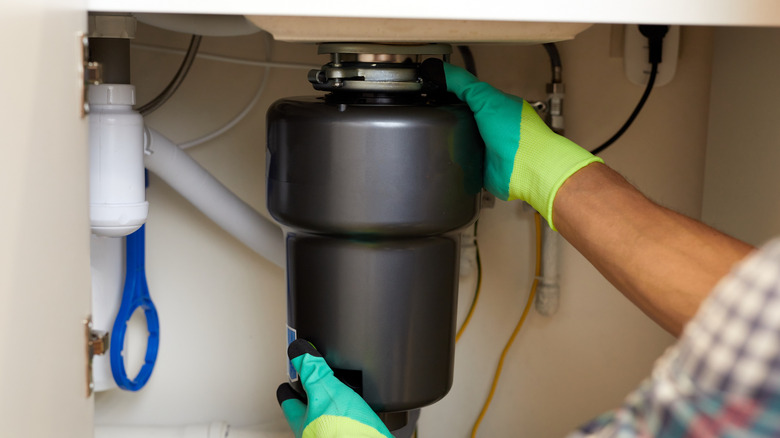man in gloves installs garbage disposal under sink