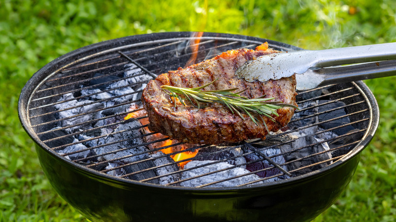 A thick cut of steak being flipped on a charcoal grill