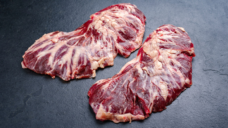 Two cuts of steak laying on a gray marble surface