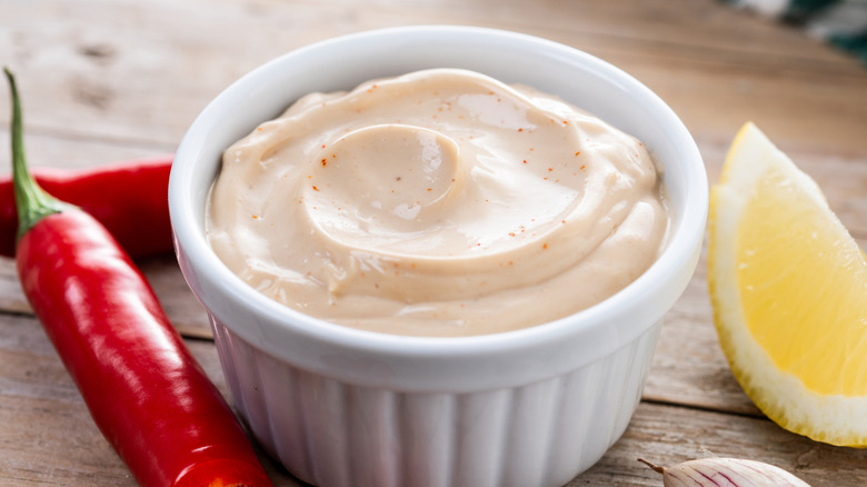 Pot of spicy mayo next to lemon wedge and fresh red chile pepper