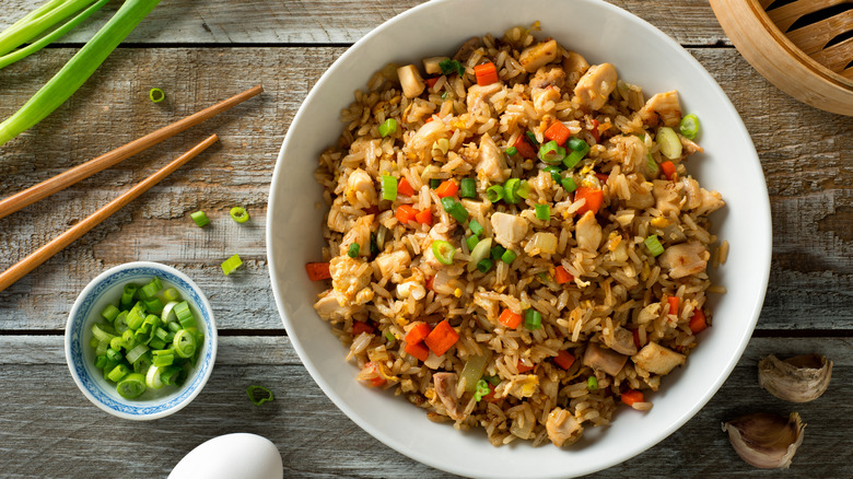 Bowl of chicken fried rice next to chopped green onion and chopsticks