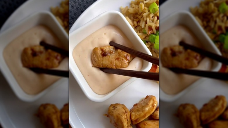 Dipping piece of chicken into bowl of yum yum sauce with chopsticks