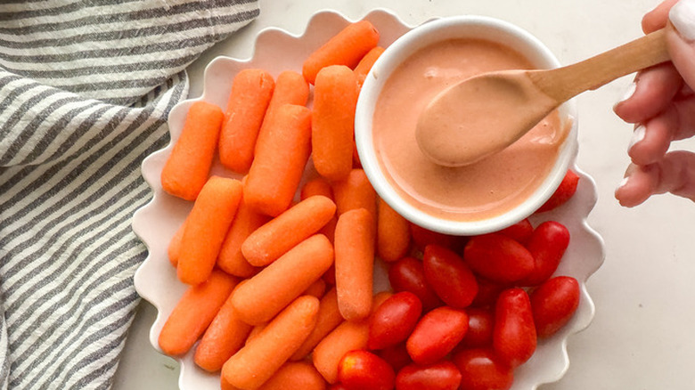 Bowl of yum yum sauce on platter of baby carrots and tomatoes