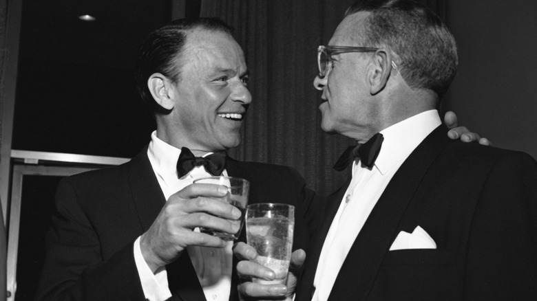 Frank Sinatra and George Burns smiling at each other while holding drinks