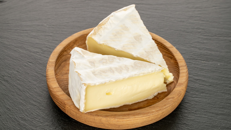 Brie cheese on wooden plate on slate stone, close-up