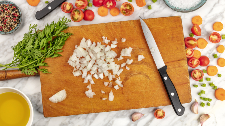 Cutting board with chopped onions and knife, tomatoes and herbs on the countertop