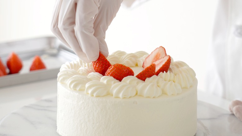 Hand putting strawberries on a cream cake