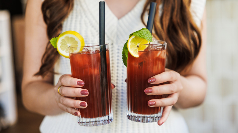 two hands holding two glasses of iced tea