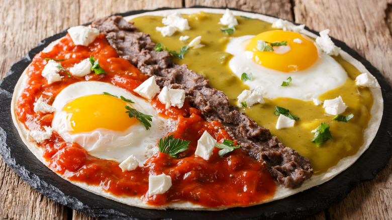 huevos divorciados separated by refried beans on rustic plate