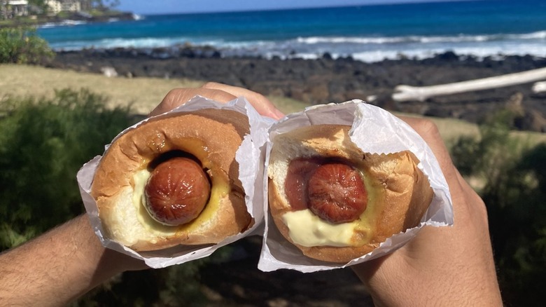 hands holding two puka dogs by the beach