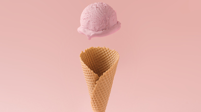Strawberry ice cream falling into a waffle cone
