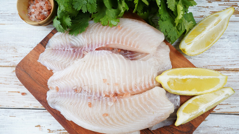 Tilapia fillets on a cutting board with lemon wedges, parsley and salt
