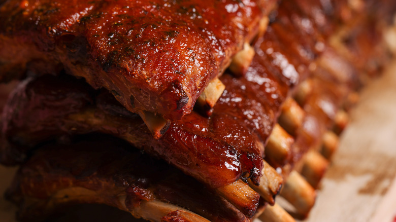 A close-up of several racks of cooked baby back ribs are piled on top of each other, with the bones visible