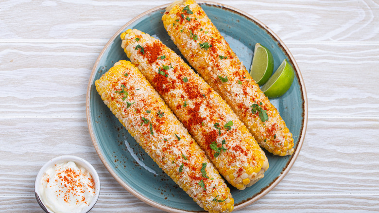 A plate of three Mexican street corn cobs topped with spices and cilantro