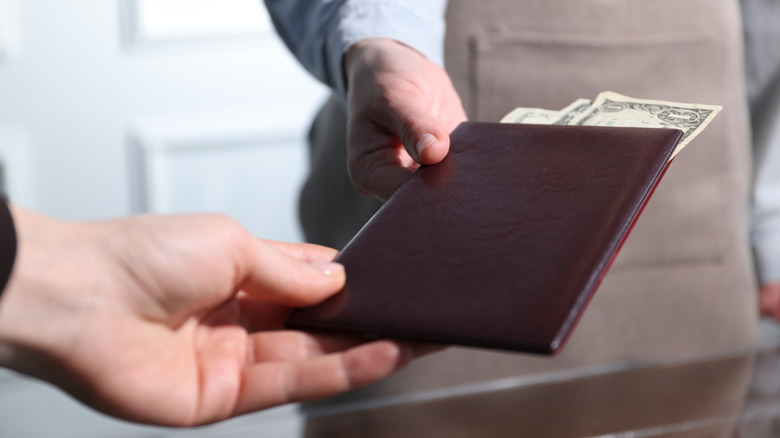 A guest hands a server a check presenter with cash sticking out
