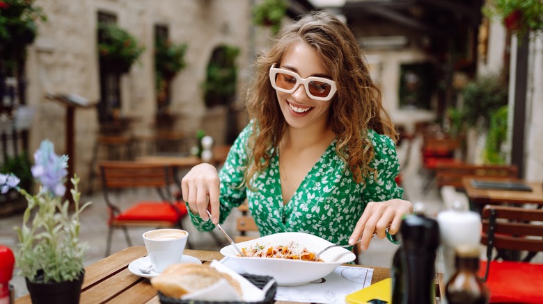 Woman eating plate of pasta outdoors smiling