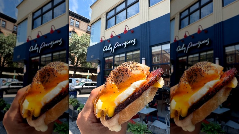 Mirrored image of hand holding breakfast sandwich in front of Daily Provisions storefront