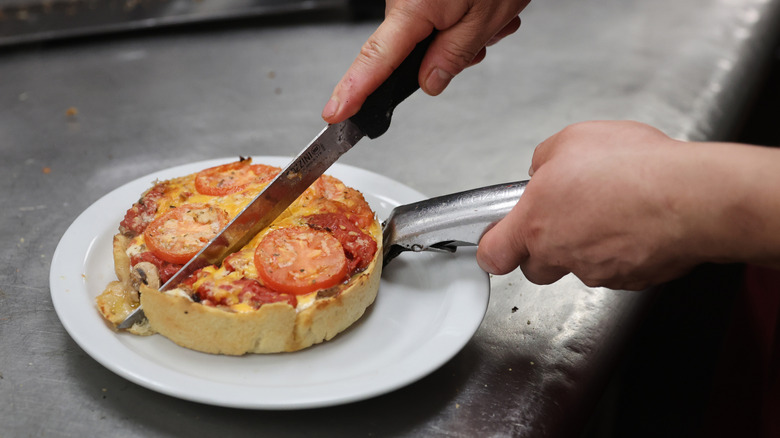 Close up of hands cutting through a Chicago-style deep dish pizza on a white plate at a Lou Malnati's restaurant