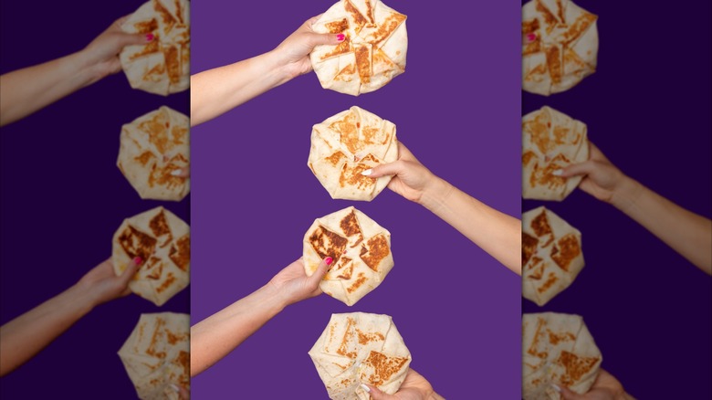 Multiple Hands holding crunchwrap supremes against purple background, mirrored image