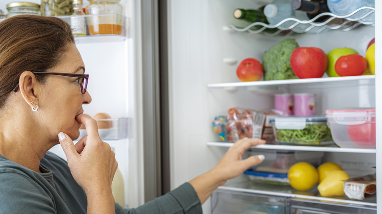 A woman looking thoughtful at the food inside her fridge
