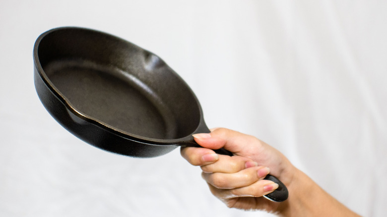 A person's arm holds up a cast iron pan