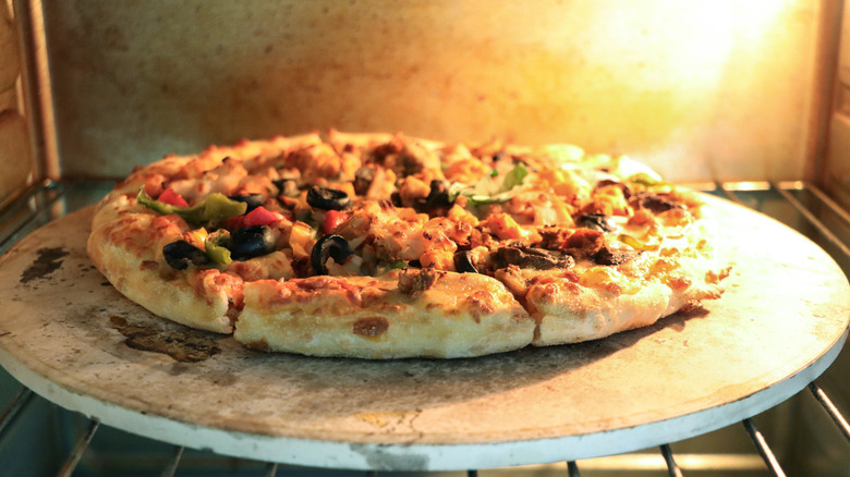 A pizza sits on a pizza stone in an oven