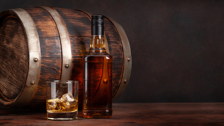 a bottle and glass of bourbon in front of barrel