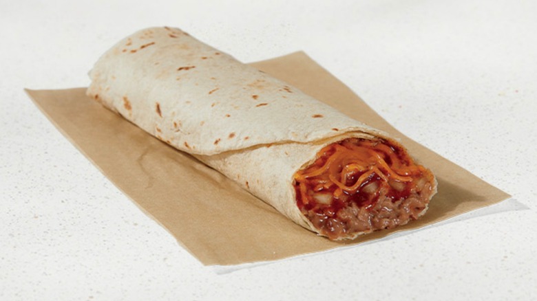 A Bean Burrito topped with red sauce, cheese, and onion on a napkin