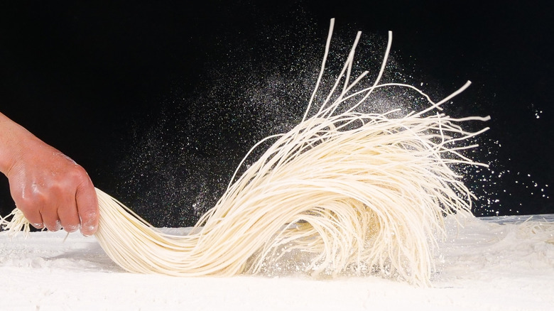 hand whipping a fistful of hand-pulled noodles against a black background